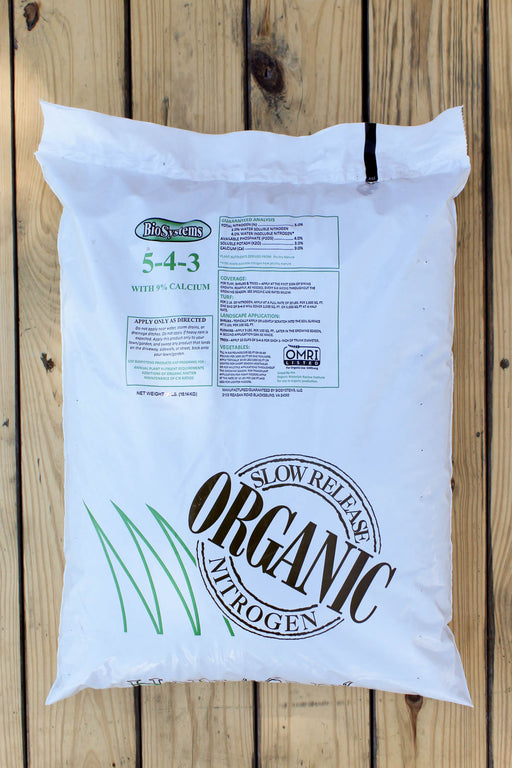 A large white bag of BioSystems Nitrogen 5-4-3 slow-release fertilizer with calcium, displayed on a light-colored wooden plank background.