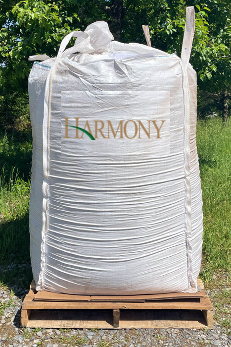 A large white bulk tote with the brand name 'HARMONY' printed on the front, resting on a wooden pallet outdoors on a gravel surface with grass and trees in the background.