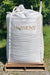 A large white bulk tote with the brand name 'HARMONY' printed on the front, resting on a wooden pallet outdoors on a gravel surface with grass and trees in the background.