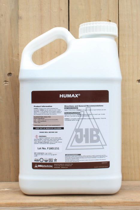 A large white plastic jug of JHB Humax liquid fertilizer with a handle, set against a rustic wooden plank background.
