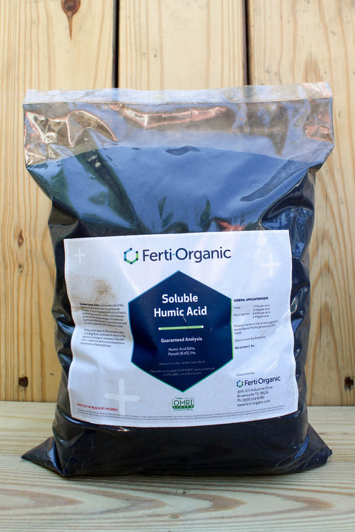 A large bag of Ferti Organic Soluble Humic Acid, filled with dark brown/black powder, standing on a wooden surface against a wooden plank background.