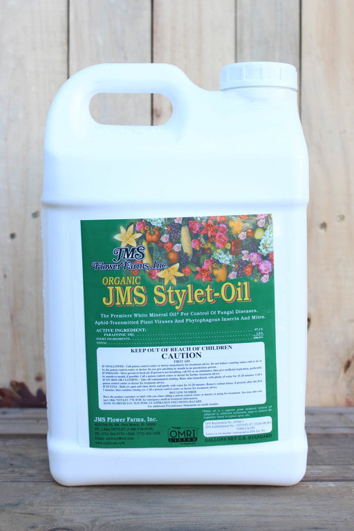 A white plastic jug of JMS Organic JMS Stylet-Oil featuring a green label with a colorful floral illustration, set against a rustic wooden background.