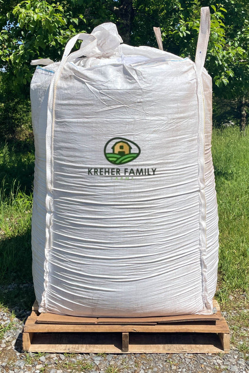 A large white bulk tote with the Kreher Family Farms logo, sitting on a wooden pallet outdoors on a grassy area with trees in the background.