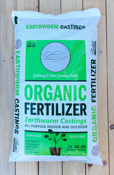 A 32 lb bag of Mountain Gate Organics Organic Fertilizer made from Earthworm Castings, displayed on a light-colored wooden plank surface.