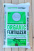 A 32 lb bag of Mountain Gate Organics Organic Fertilizer made from Earthworm Castings, displayed on a light-colored wooden plank surface.