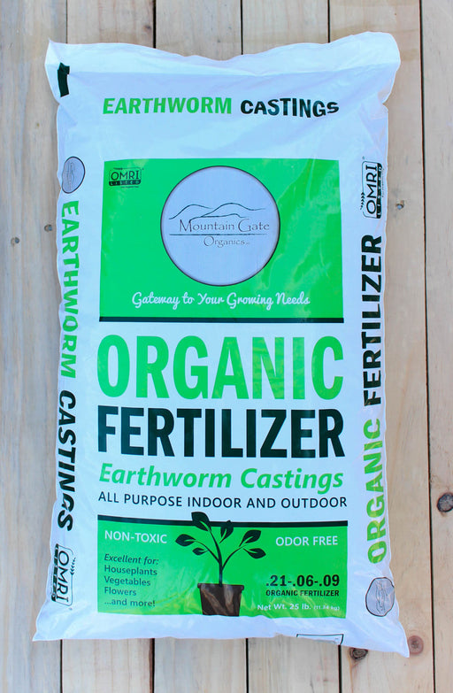 A 32 lb bag of Mountain Gate Organics Organic Fertilizer made from Earthworm Castings, displayed on a light-colored wooden plank surface.