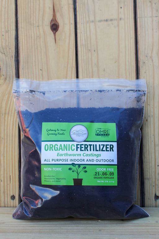 A bag of Organic Fertilizer Earthworm Castings by MGO, placed on a wooden surface against a wooden plank background.