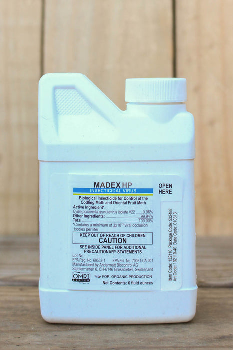 A small white plastic bottle of Madex HP Insecticidal Virus, standing upright on a wooden surface with a blurred wood background.