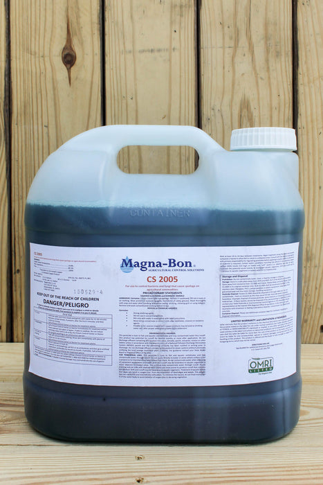 A large plastic jug of Magna-Bon CS 2005 with a white label and white cap, set against a rustic wooden plank background.
