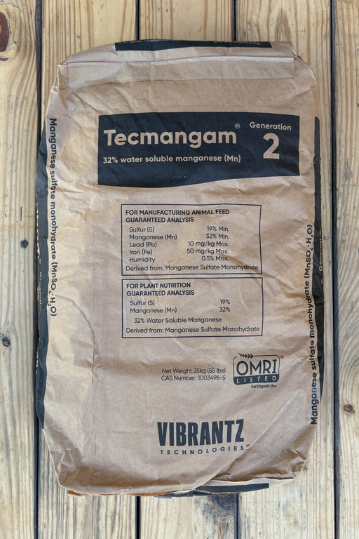 A brown paper bag of Vibrantz Technologies Tecmangam manganese sulfate monohydrate, displayed flat on a light-colored wooden plank surface.