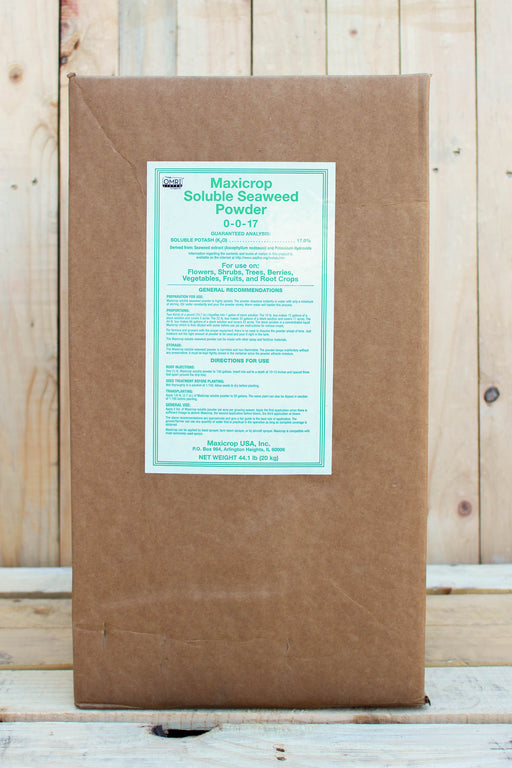 A large brown kraft paper box of Maxicrop Soluble Seaweed Powder 0-0-17, featuring a white label with green text, set against a rustic light wood plank background.