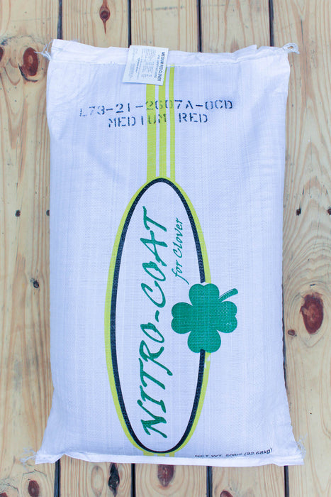 A white bag of Clover Nitro-Coat medium red clover, displayed flat on a light-colored wooden plank surface.