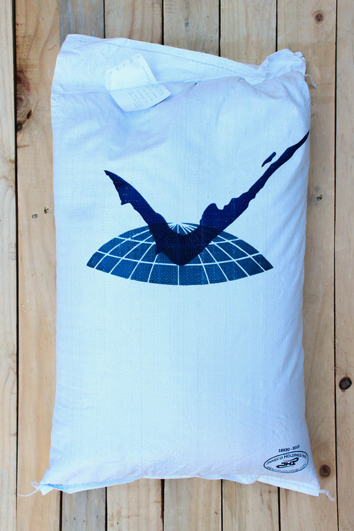 A large white sack with a dark blue graphic of a diving figure on a grid dome, placed on a light wood plank surface. A small circular logo is visible in the bottom right corner.