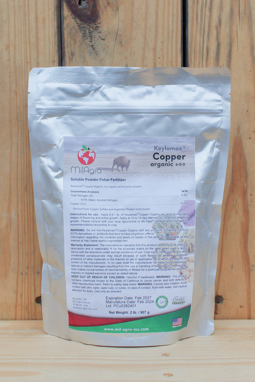A silver stand-up pouch of MilAgro Keylamax Copper Organic Fertilizer, displayed against a rustic wooden plank background.
