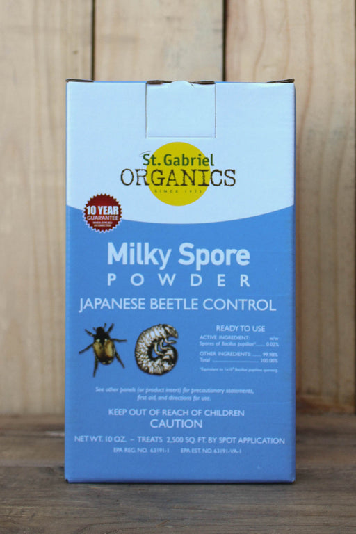A blue and white box of St. Gabriel Organics Milky Spore Powder for Japanese Beetle Control, displayed on a wooden surface against a wooden background.