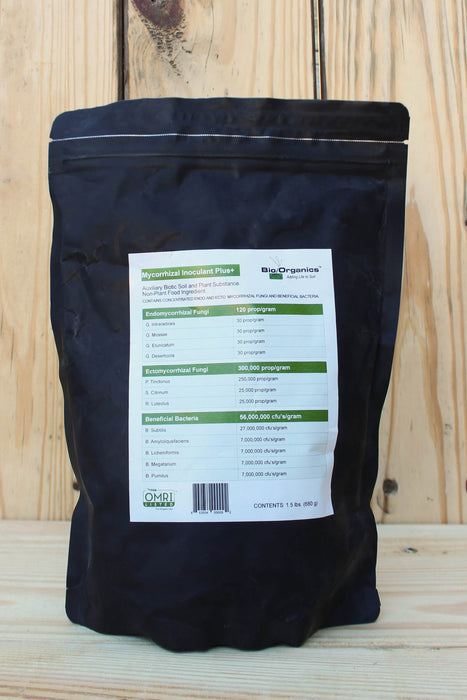 A black stand-up pouch of Mycorrhizal Inoculant Plus+, showing the back label with text and a barcode, set against a light wood plank background.