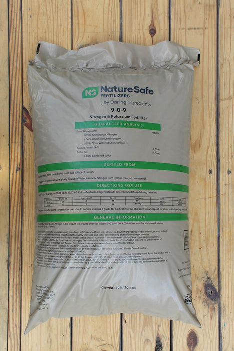 A large bag of Nature Safe Fertilizers 9-0-9 Nitrogen & Potassium Fertilizer, displayed flat on a light-colored wooden plank surface.