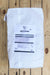 A white paper bag with a printed Nature Safe label, placed on a light-colored wooden plank surface.