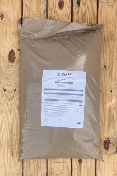 A large brown plastic bag of NatureSafe Organic Fertilizer with a white label, placed on a light-colored wooden plank surface.