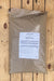 A large brown plastic bag of NatureSafe Organic Fertilizer with a white label, placed on a light-colored wooden plank surface.