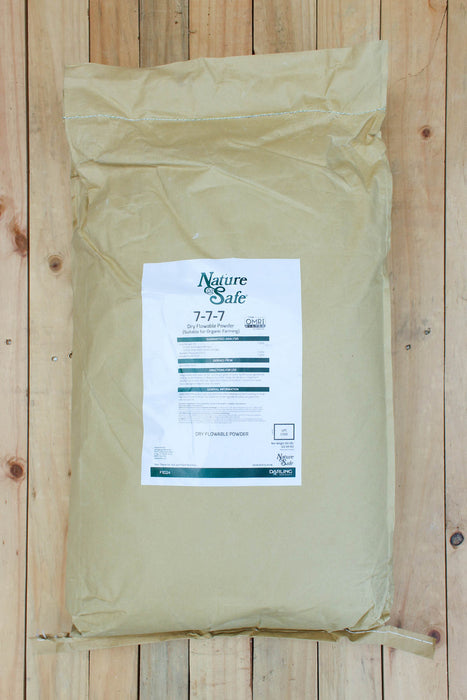 A large beige paper bag of Nature's Safe 7-7-7 fertilizer, displayed flat on a light-colored wooden plank surface.