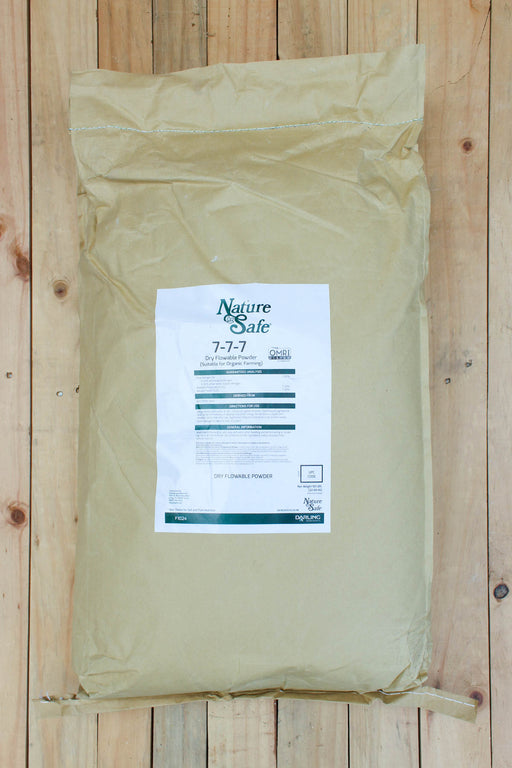 A large beige paper bag of Nature's Safe 7-7-7 fertilizer, displayed flat on a light-colored wooden plank surface.