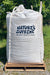 A large white plastic tote of Nature's Supreme Plant Fertilizer sitting on a wooden pallet outdoors on a gravel surface with green grass and trees in the background.