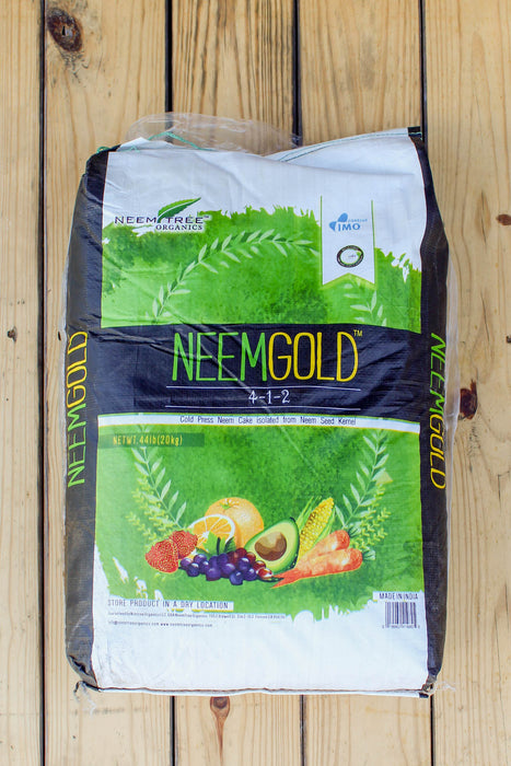 A bag of NeemGold 3-1-2 fertilizer by NeemTree Agro Products, placed on a light-colored wooden plank surface. The bag is white and black with prominent green and yellow branding and illustrations of fruits at the bottom.