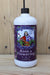 A white plastic bottle of Neptune's Harvest Rose & Flowering fertilizer with a black cap, set against a light wood plank background.