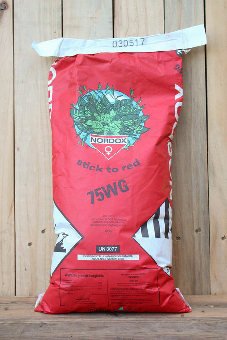 A red and white bag of Nordox 75WG, standing upright against a light-colored wooden plank wall.