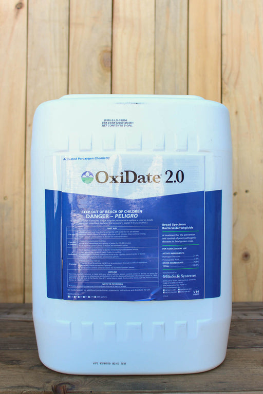 A large white plastic bucket of OxiDate 2.0, featuring a blue and white label, set against a rustic wooden plank background.