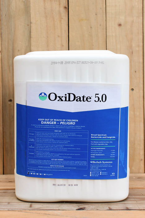 A large white plastic bucket of OxiDate 5.0 liquid oxidizer with a blue and white label, set against a rustic wooden plank background.