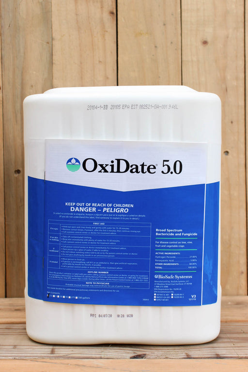 A large white plastic bucket of OxiDate 5.0 liquid oxidizer with a blue and white label, set against a rustic wooden plank background.