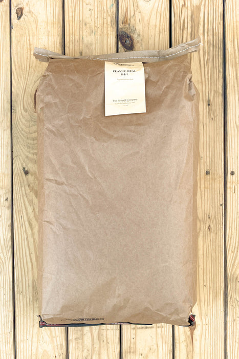 A brown kraft paper bag with a white paper label reading 'Peanut Meal', laid flat on a light wood plank background.