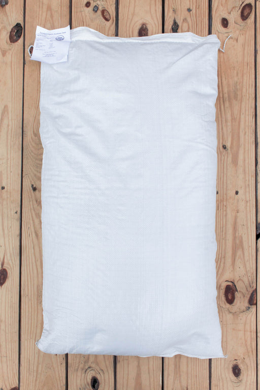 A plain white bag of Peredovik Sunflower seeds laid flat on a light wood plank surface.