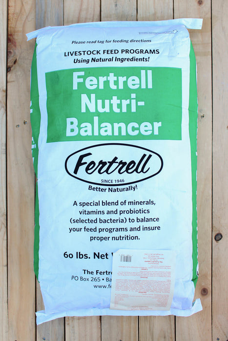 A 60 lb bag of Fertrell Nutri-Balancer livestock feed program supplement, displayed flat on a light-colored wooden plank surface. The bag is white with a prominent green label block and black text.