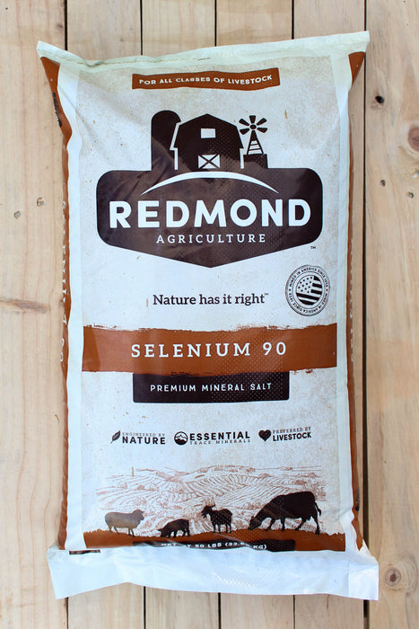 A large bag of Redmond Agriculture Selenium 90 Premium Mineral Salt for all classes of livestock, displayed flat on a light-colored wooden plank surface.