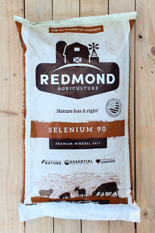 A large bag of Redmond Agriculture Selenium 90 Premium Mineral Salt for all classes of livestock, displayed flat on a light-colored wooden plank surface.