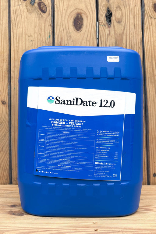 A large blue plastic jug of SaniDate 12.0 standing upright against a rustic wooden plank background.