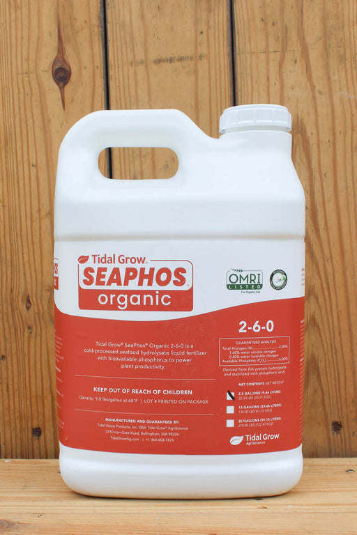 A white plastic jug of Tidal Grow Seaphos Organic 2-6-0 liquid fertilizer with a prominent red label, set against a rustic wooden plank background.