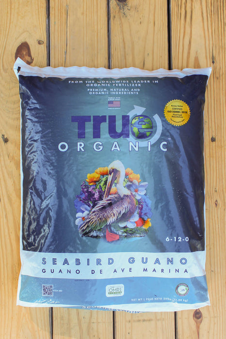 A large bag of True Organic Seabird Guano (Guano de Ave Marina) displayed flat on a light-colored wooden plank surface.