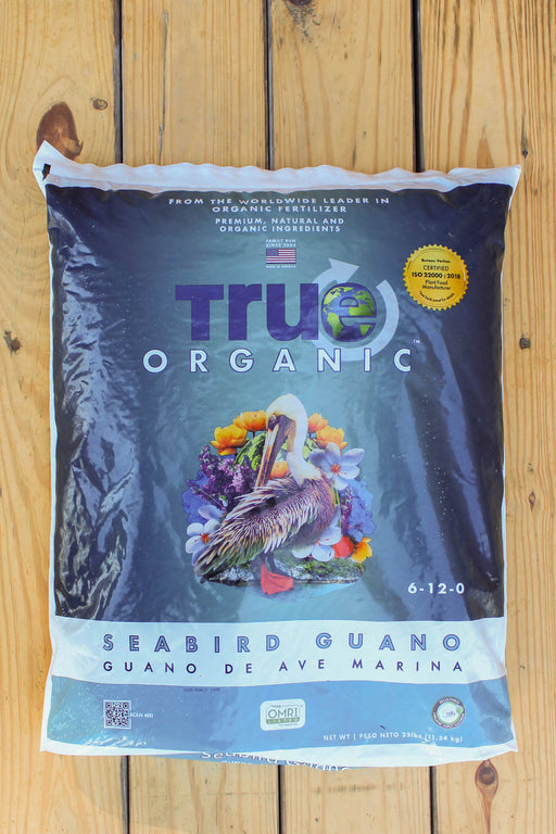 A large bag of True Organic Seabird Guano (Guano de Ave Marina) displayed flat on a light-colored wooden plank surface.