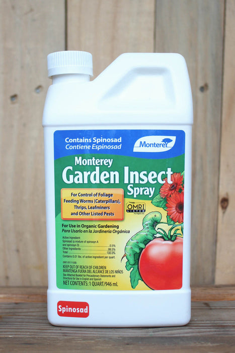A white plastic bottle of Monterey Garden Insect Spray with a colorful label, set against a rustic wooden plank background.