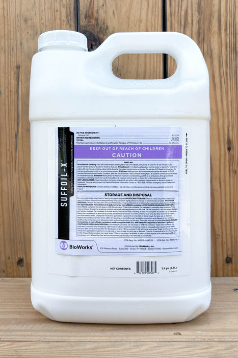A large white plastic jug of BioWorks SUFFOIL-X with a detailed product label, set against a rustic wooden plank background.