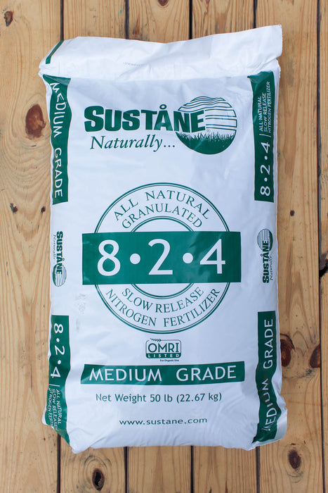 A 50 lb bag of Sustane 8-2-4 Medium Grade slow release nitrogen fertilizer, shown flat on a light brown wooden plank background.
