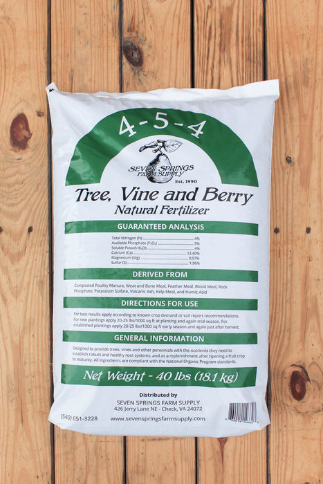 A 40 lbs bag of Seven Springs Farm Supply Tree, Vine and Berry Natural Fertilizer, displayed on a light brown wooden plank background.