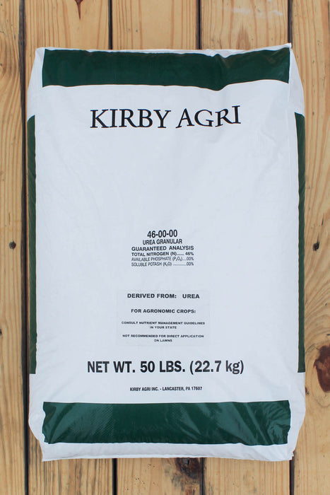 A 50 lb bag of Kirby Agri 46-50-00 Urea Granules, laid flat on a light-colored wooden plank surface. The bag is white with dark green bands at the top and bottom, and black text detailing the product name, ingredients, and net weight.