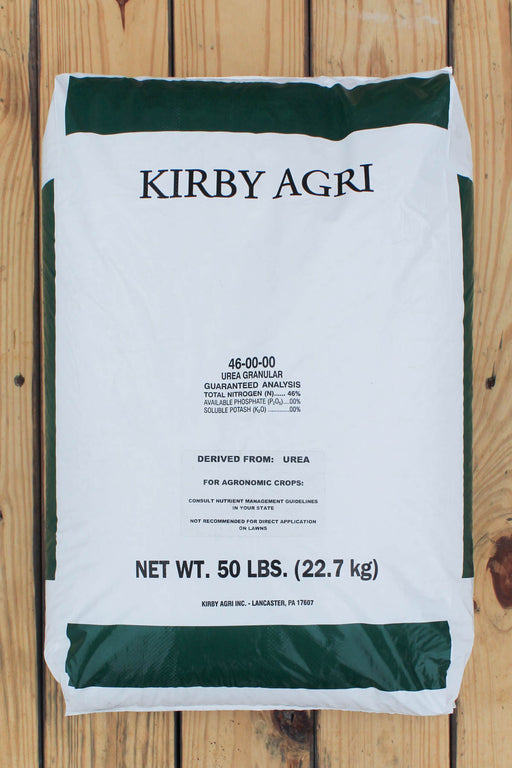 A 50 lb bag of Kirby Agri 46-50-00 Urea Granules, laid flat on a light-colored wooden plank surface. The bag is white with dark green bands at the top and bottom, and black text detailing the product name, ingredients, and net weight.