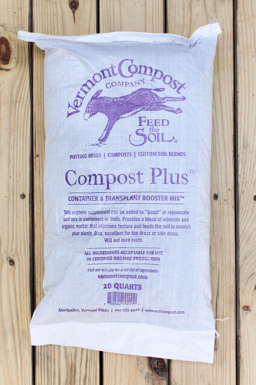 A white bag of Vermont Compost Company Compost Plus container and transplant booster mix, displayed flat against a light-colored wooden plank background.