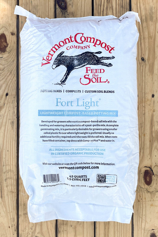 A white bag of Vermont Compost Company Fort Light compost, displayed flat on a rustic wooden plank background.